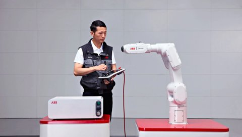 一名工程师正在用平板控制器编程ABB IRB 1200机械臂。